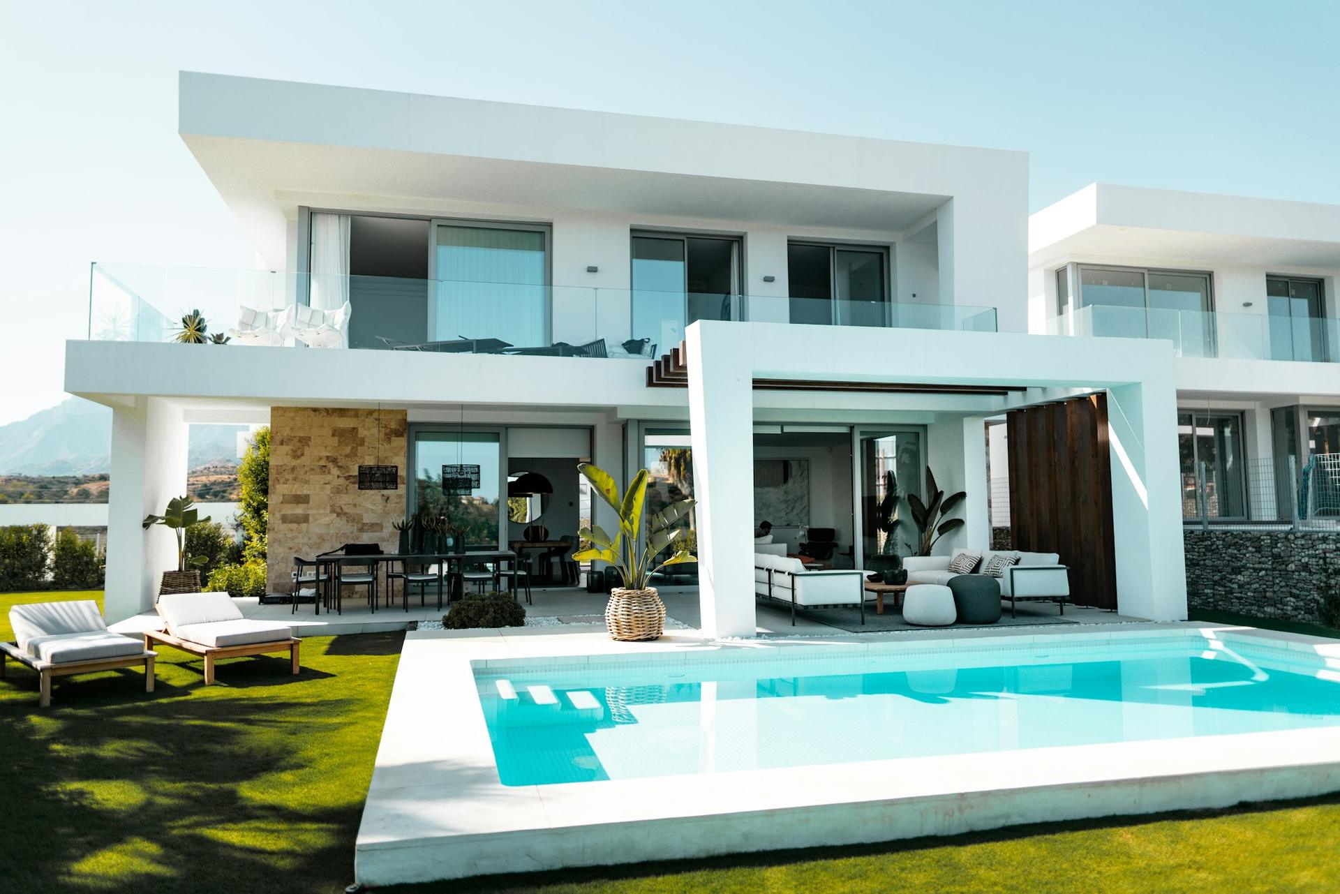 A white modernist villa with floor-to-ceiling glass, a stone-clad wall and a turquoise pool set in a manicured lawn